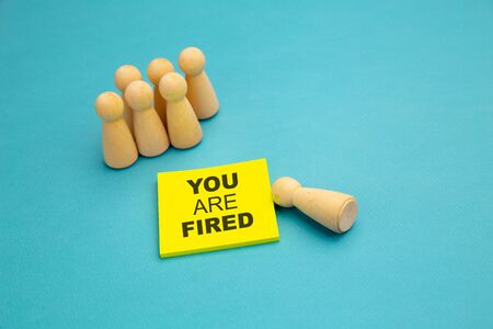 Wooden pawns near yellow sticky note with phrase "You are Fired". Unemployment conceptの写真素材