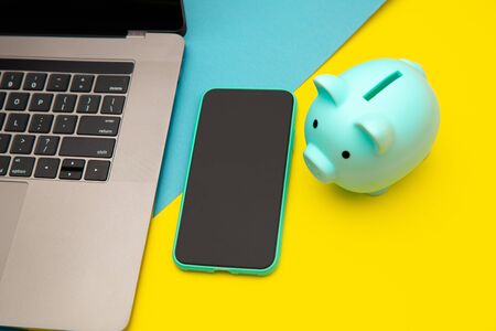 Moneybox near laptop and smartphone, place for text. Finance and budget concept. Piggy bank in pink...