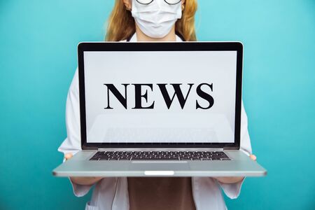 Medical news. Woman therapist in glasses holding laptop standing at the blue wall.の写真素材