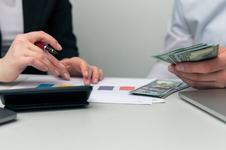 Counting money in office. Professional account on laptop and calculator.