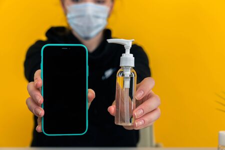 Closeup picture of female holding phone and sanitizer isolated over the yellow background.
