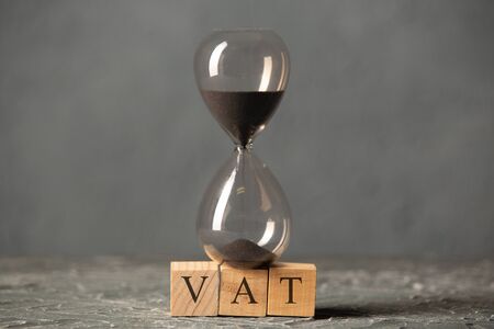 Hourglass or sandglass on cube wooden block with alphabets VAT, Value Added Tax on the table.