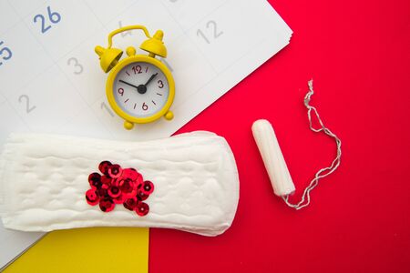 Menstrual calendar with feminine products and alarm clock on colorful backgroundの写真素材