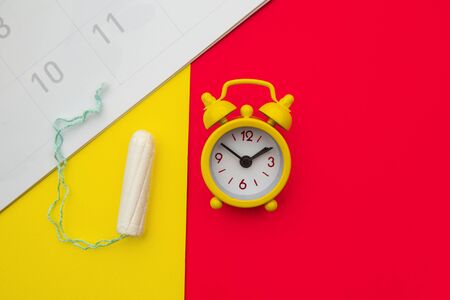 Menstrual calendar, cotton tampon and alarm clock on colorful background. Females menstrual cycle conceptの写真素材
