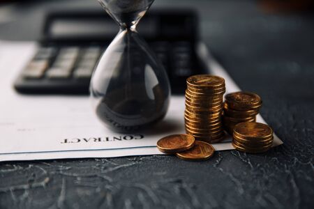 Time is money concept. Signing a contract. Coins and hourglass next to the calculator on a contract