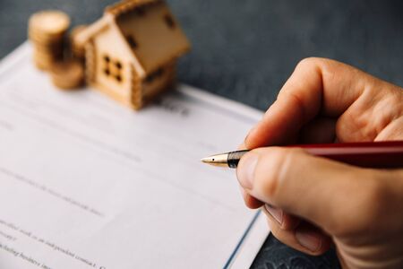 Image of a man signing a mortgage or insurance contract or the deed of sale when buying a new house or selling his existing one with a small wooden model of houseの写真素材