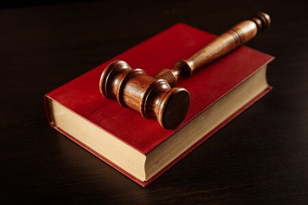 law book with a judges gavel resting on top of the pages in a courtroom or law enforcement office.