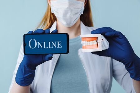 Portrait of beautiful female dentist posing in dental clinic holding smartphone with green screen and presenting mobile app or website to camera, copy space.の写真素材