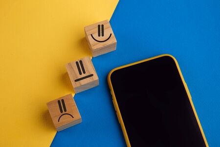 Emotion face symbol on wooden cube blocks and smartphone. Service rating, ranking, customer review, satisfaction and feedback conceptの写真素材