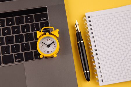 Home office workplace desk concept. Laptop, clock, notebook and pen on yellow backgroundの写真素材