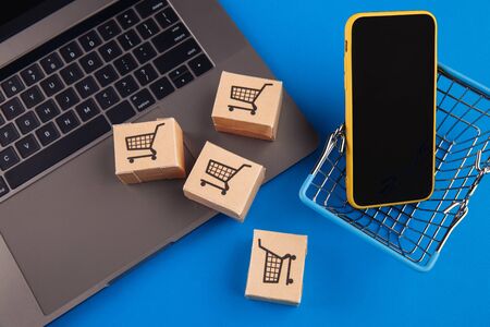 Top view on a shopping basket, boxes and mobile phone on a blue background. Smartphone online shopping conceptの写真素材