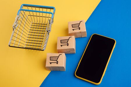 Online shopping concept. Smartphone with mini boxes and shopping basket on blue yellow background