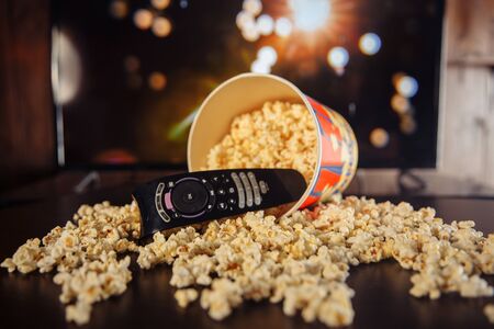 Craft bowl of popcorn on the dark table and TV remote control with TV set.の写真素材