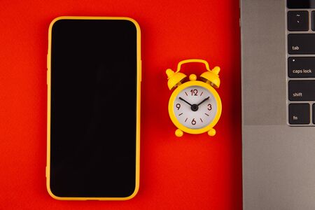 Home office workplace desk concept. Laptop, smartphone and clock on red background close up.の写真素材