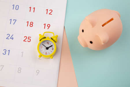 Savings concept. Piggy bank and alarm clock with calendar on colorful background