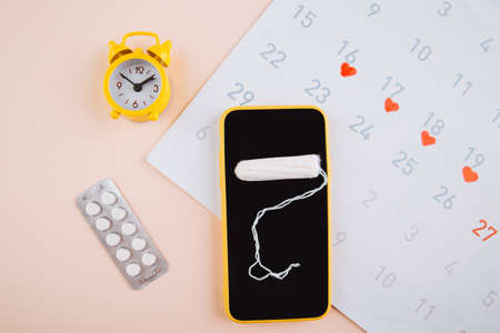 Mobile application to track your menstrual cycle and for marks. PMS and the critical days concept. Cotton tampon and yellow alarm clock on the pink backgroundの写真素材