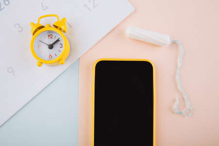 Menstrual cycle concept. Yellow alarm clock and a mobile application on the smartphone screen....