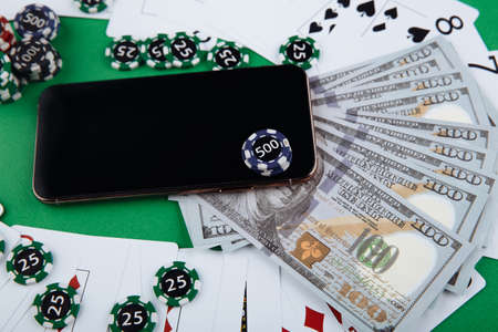 Online casino concept, playing cards, money, dice chips and smartphone with copyspace on the green table.の写真素材