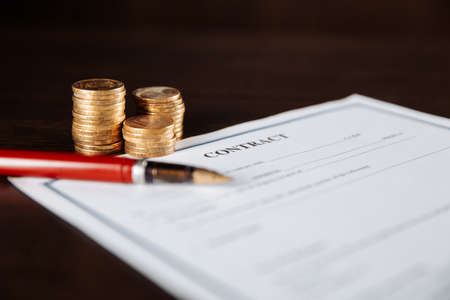 Signing a contract, pen and coins on a wooden tableの写真素材