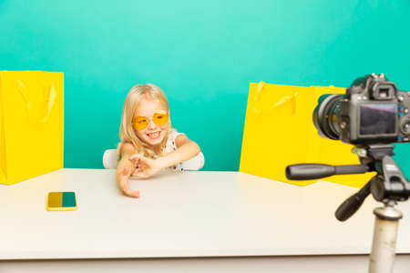 Happy girl at home speaking in front of camera for vlog. Little kid working as blogger, recording...