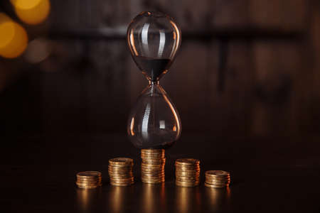 Sand clock with stack of coins. Time is money, investment concept