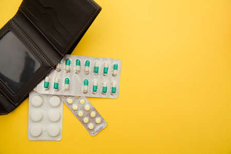 Empty wallet with tablets of pills on yellow backgroundの写真素材