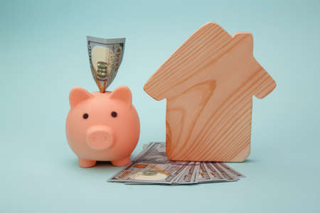 Piggy bank with model of house and money banknotes on blue background. Savings money for buy houseの写真素材