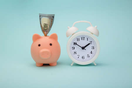 Piggy bank with money banknotes and alarm clock on blue background. Time is money conceptの写真素材
