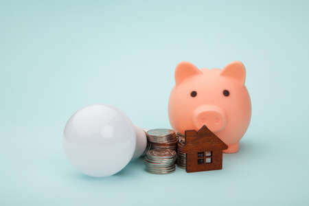 Piggy bank with money banknote and led light bulb, house figure on blue background. Power saving conceptの写真素材