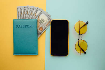 Travel planning with smartphone, sunglasses and passport with money on blue yellow backgroundの写真素材