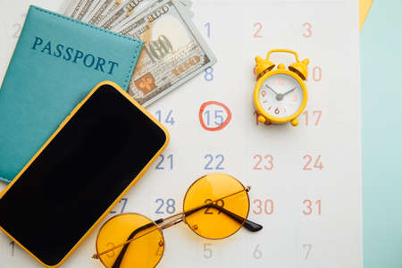 Calendar with passport, sunglasses and smartphone on blue background. Vacation planning conceptの写真素材