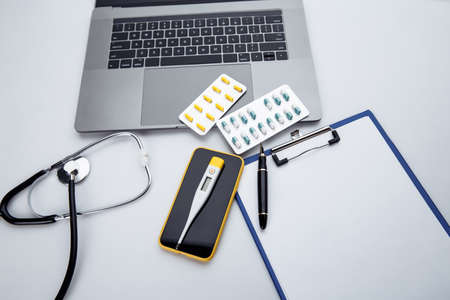 Medical desktop with stethoscope, pills, thermometer, smartphone and laptop keyboardの写真素材