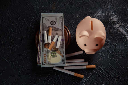 Piggy bank and cigarettes on grey background. Expensive and harmful habit