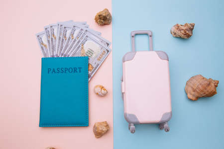 Pink suitcase and passport with money on blue pink background with shells. Travel, summer vacation...