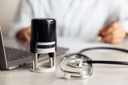 Doctor is sitting at table and signing medical document in officeの写真素材