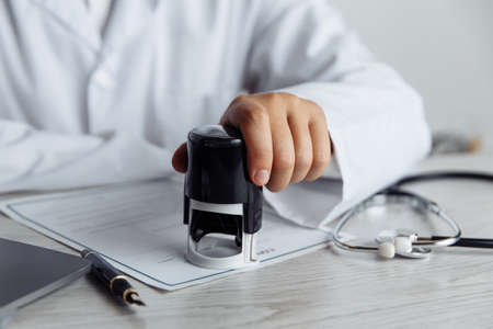 Male doctor in public medical office is stamping medical document. Healthcare conceptの写真素材