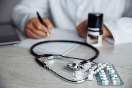 Doctor writing information to patient on medicine paper in officeの写真素材