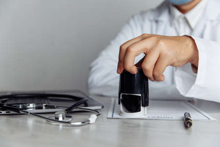 Male doctor in office is stamping medical document, close-up hand. Medicine conceptの写真素材