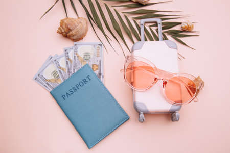 Passport with money, sunglasses and pink suitcase on pink background with shells. Top view. Summer vacation preparation conceptの写真素材