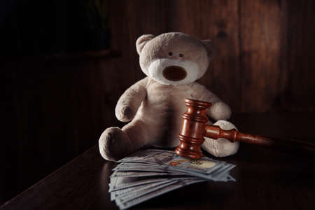 Divorce and alimony concept. Wooden gavel, dollar banknotes and teddy bear as symbol of childの写真素材