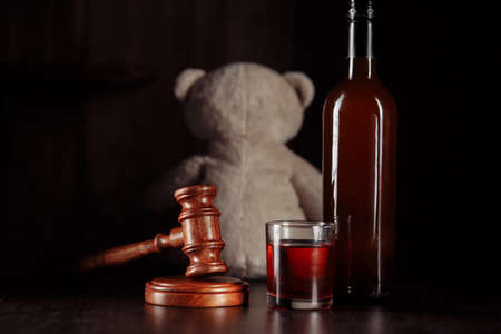 Alcohol in family and child abuse concept. Teddy bear as a symbol of childs safety, judge gavel and bottle with glassの写真素材