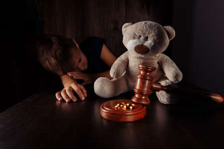 Divorce and separation concept. Wooden gavel, rings and sorrowful little boy with teddy bearの写真素材