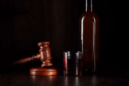 Bottle and glass with whisky and judge gavel, alcohol and crimes concept