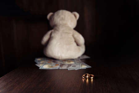 Dollar banknotes, rings and teddy bear on a wooden table. Divorce and alimony conceptの写真素材
