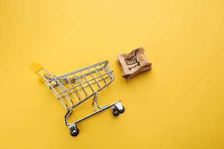 Damaged paper box and shopping cart on a yellow table. Online shopping, service and delivery conceptの写真素材