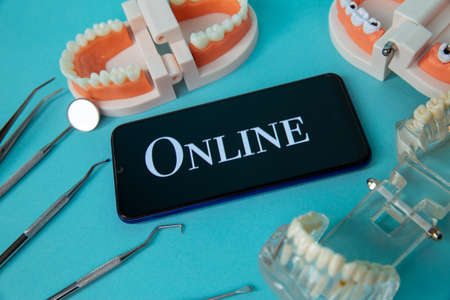 Dentist online appointment. Phone with medical instruments and jaw isolated on the blue background.の写真素材