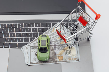 Toy car and shopping cart with dollar banknotes on a laptop. Online purchase car conceptの写真素材