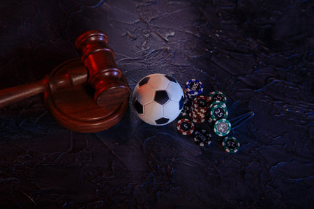 Online gambling and justice theme, soccer ball, playing chips and judge wooden gavel on a grey...