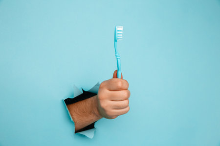 Hand showing a tooth brush out of a hole torn in blue paper wall. Health care conceptの写真素材