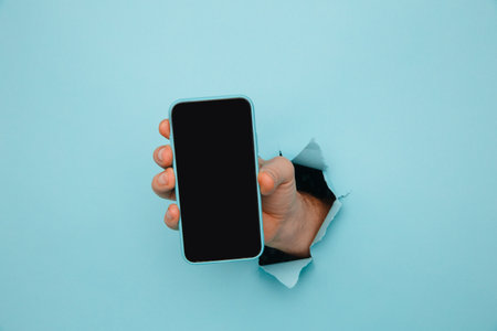Mans hand holding phone from blue torn paper